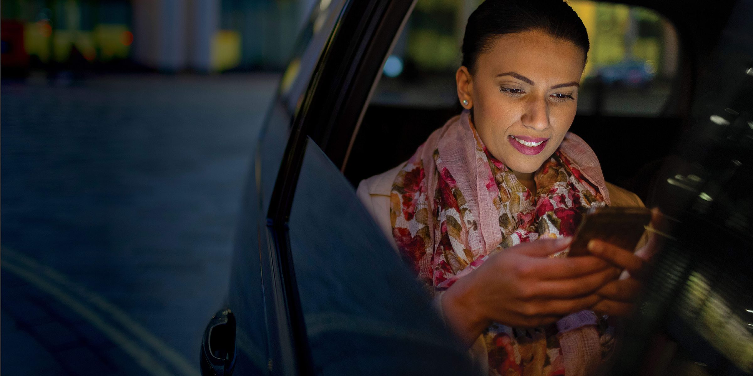 woman looking at phone while riding in car at night