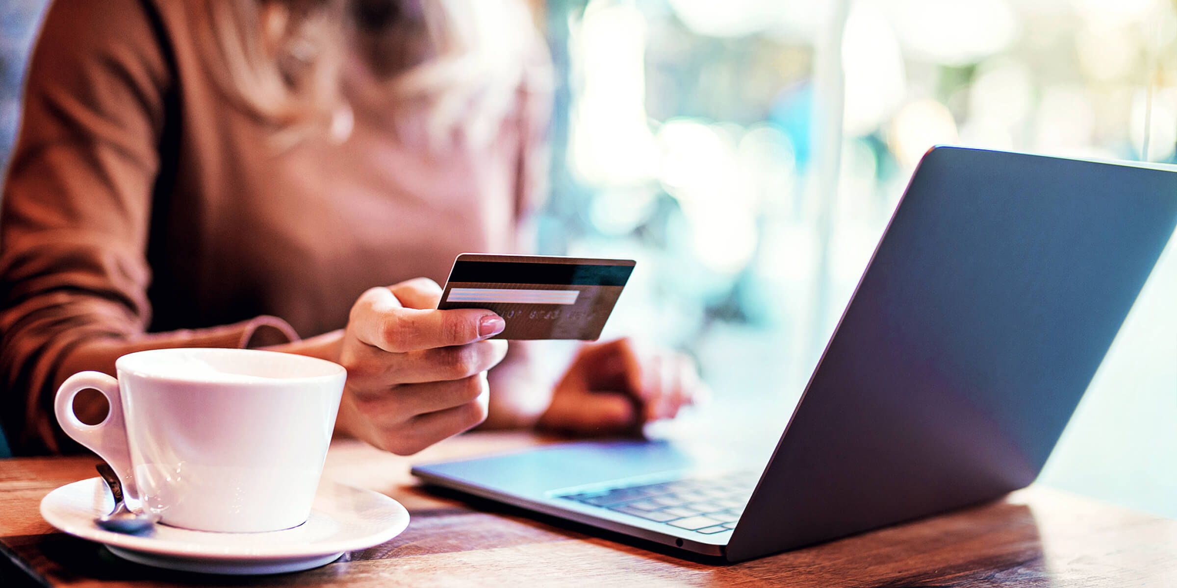 woman holding credit card sitting in front of laptop with coffee