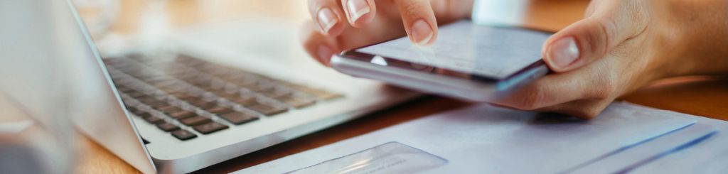 hand holding phone next to laptop