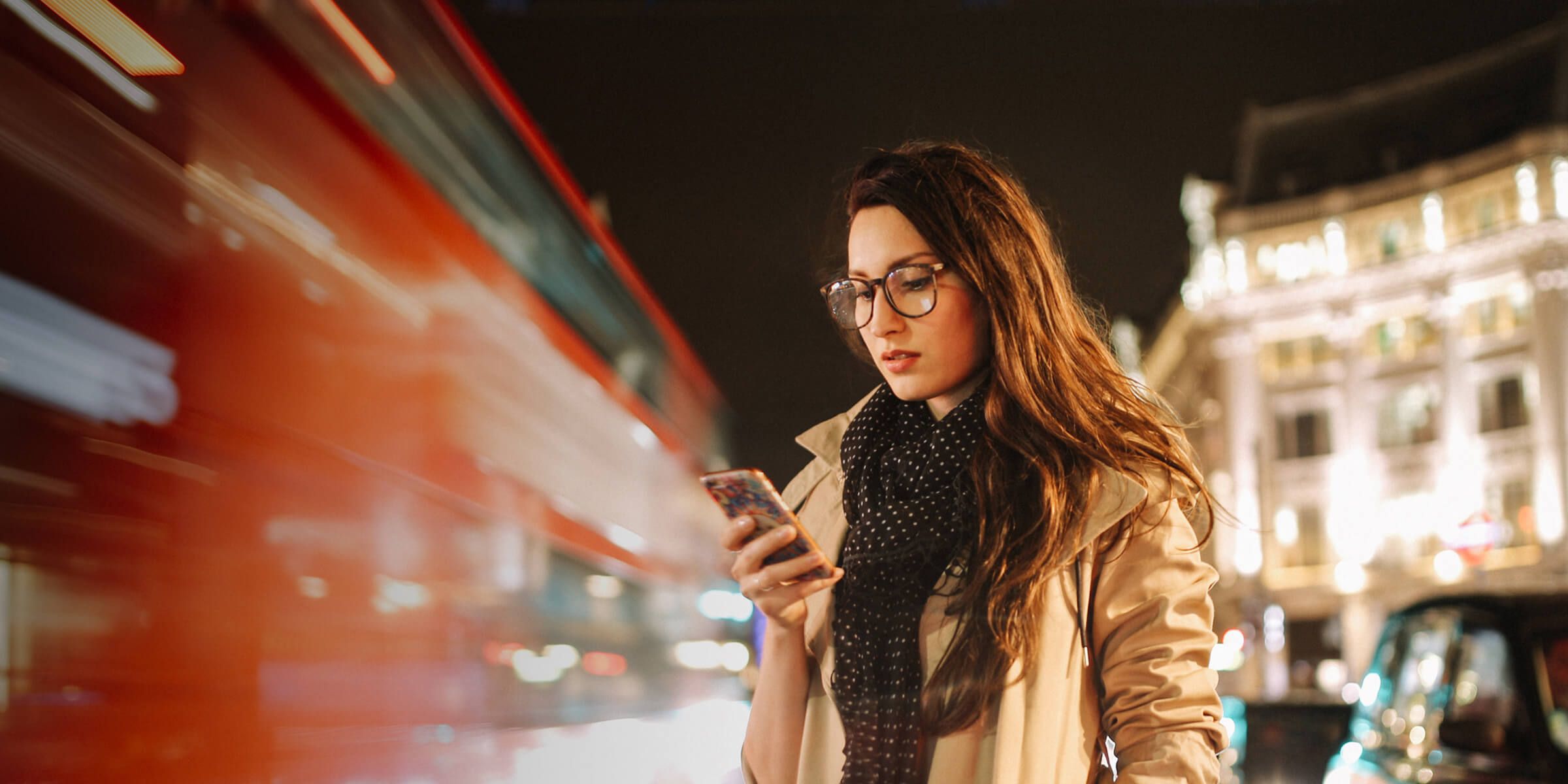 person looking at phone with blurred bus passing by her