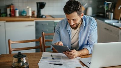 man sitting at kitchen table smiling and looking at tablet