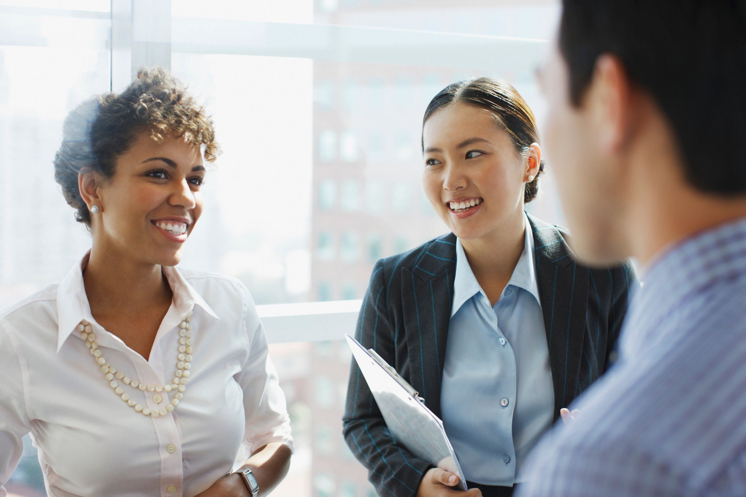 Group of diverse Fiserv Employees in office attire and having a nice conversation, two are female presenting individuals smiling at a male-presenting individual