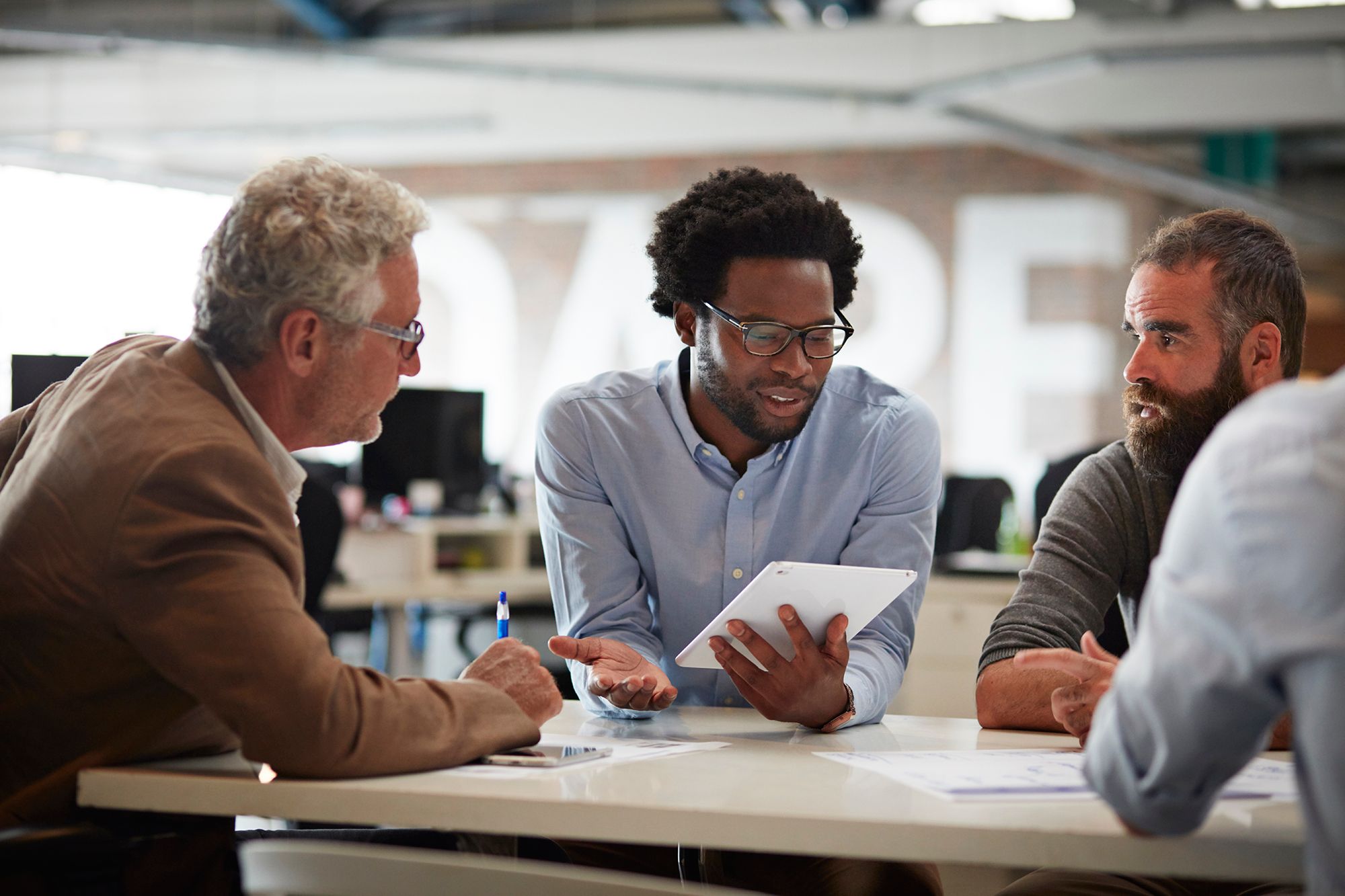 man on tablet talking to two other men