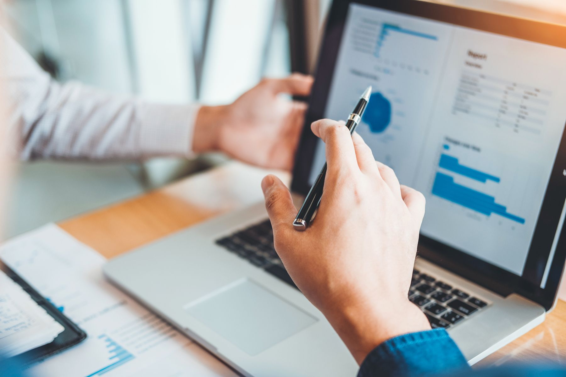 business person typing on laptop with data and charts on the screen