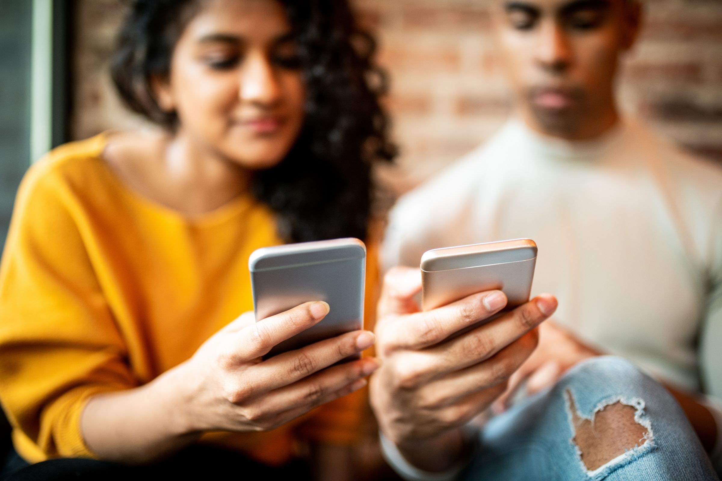 woman and man sitting next to eachother looking at their smartphones