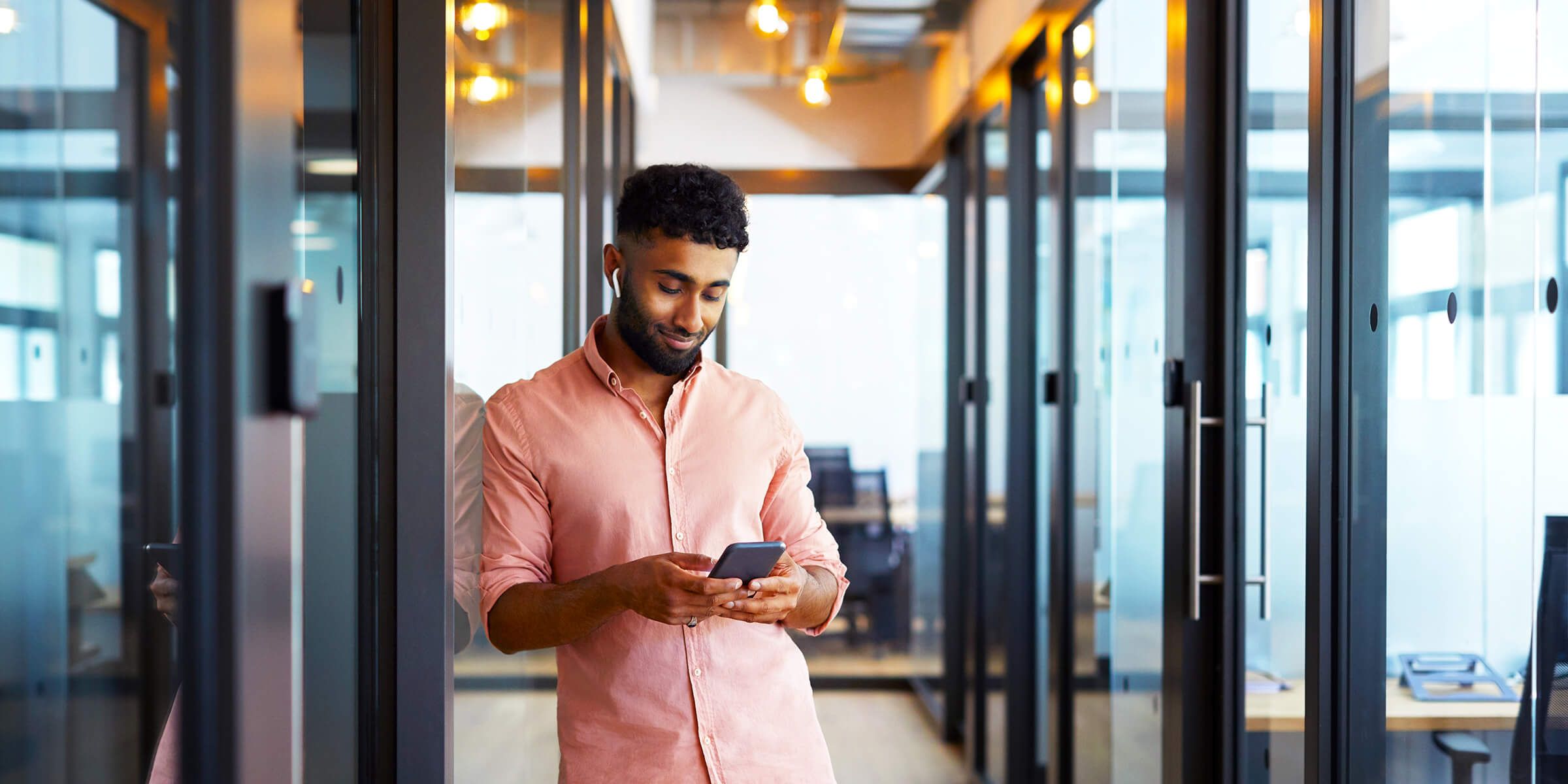 young man in office hallway looking at phone and smiling