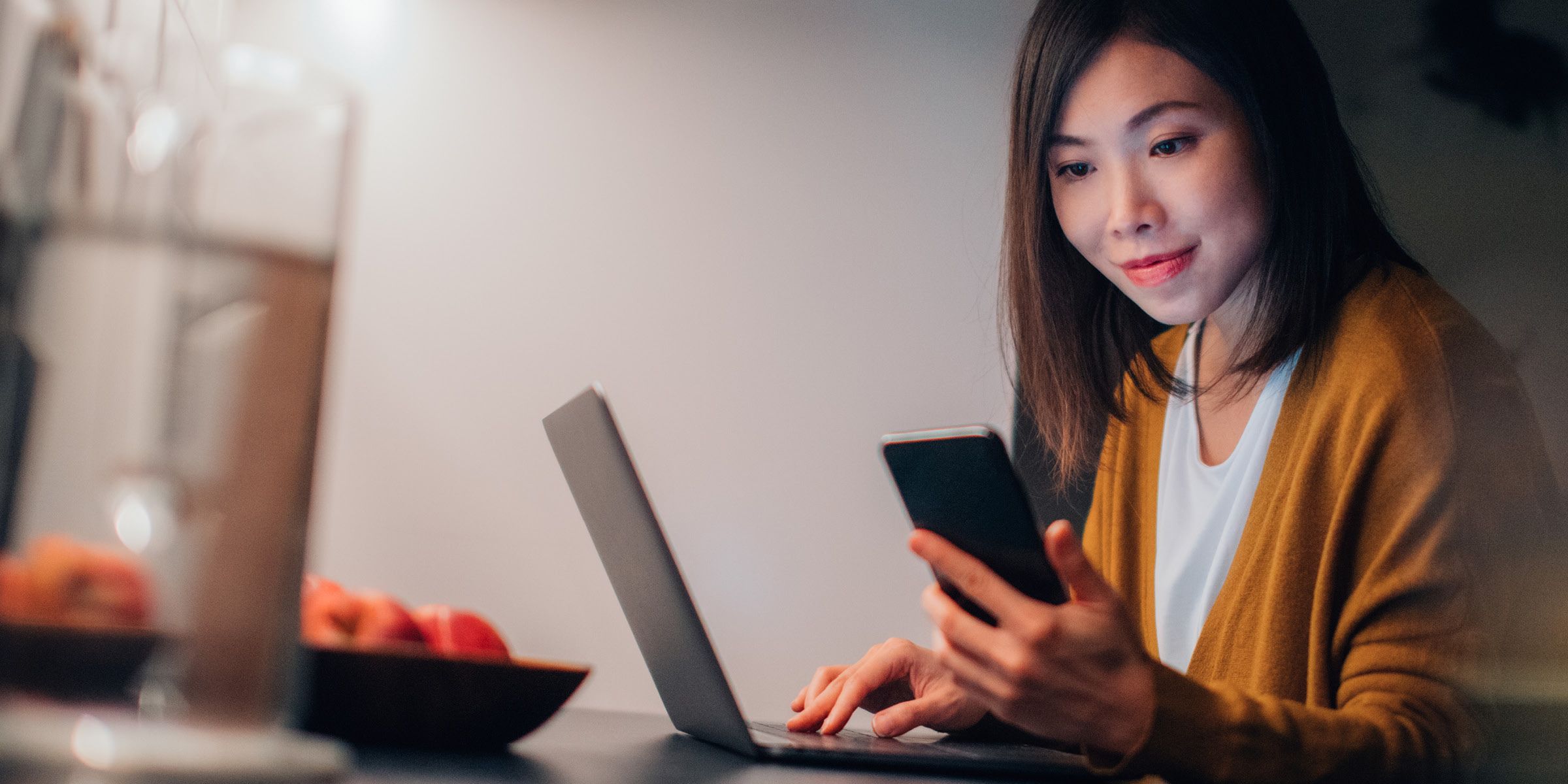 a woman looking at a phone and a laptop