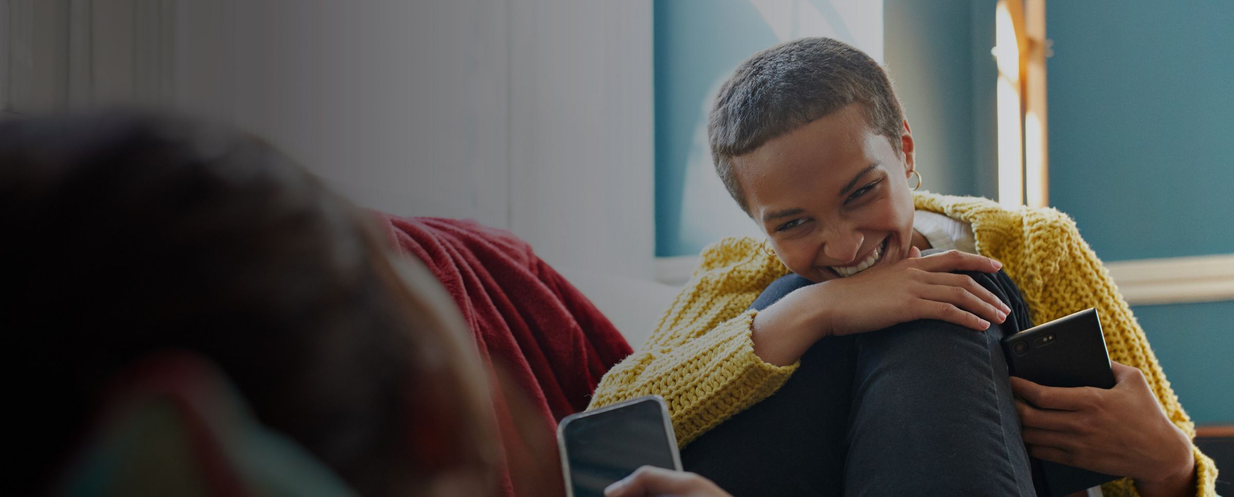 Smiling person sitting indoors holding a phone
