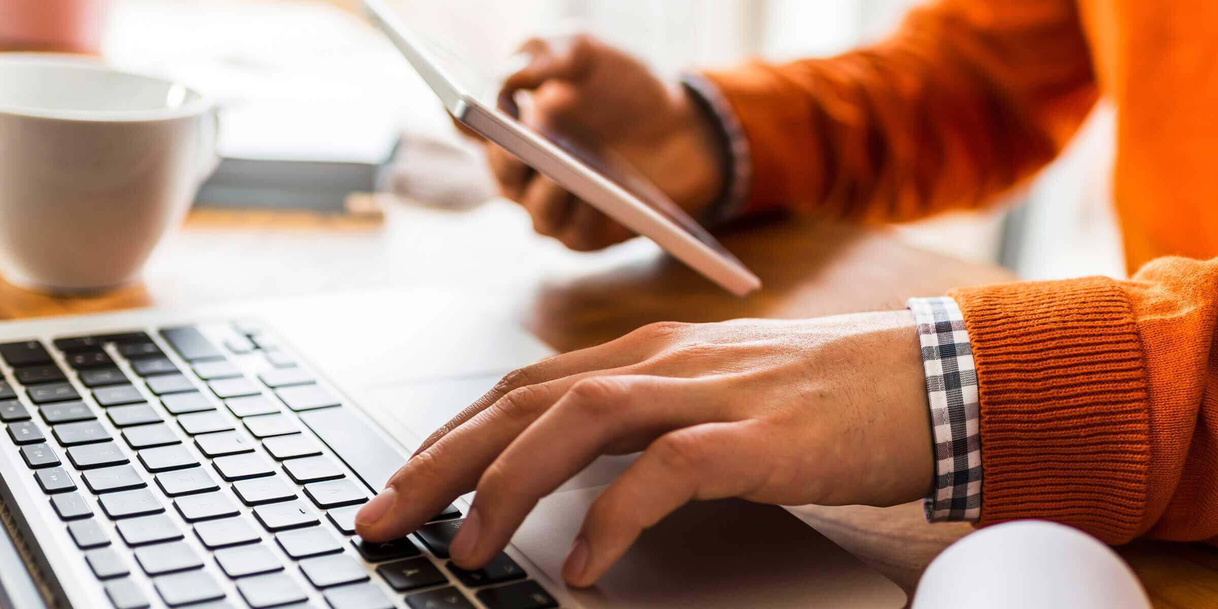 person typing on a laptop holding a phone with the other hand