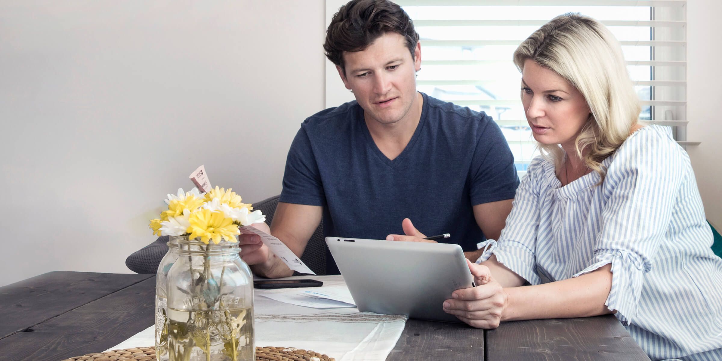 two individuals at a table with paperwork and a digital tablet, with a vase of yellow flower