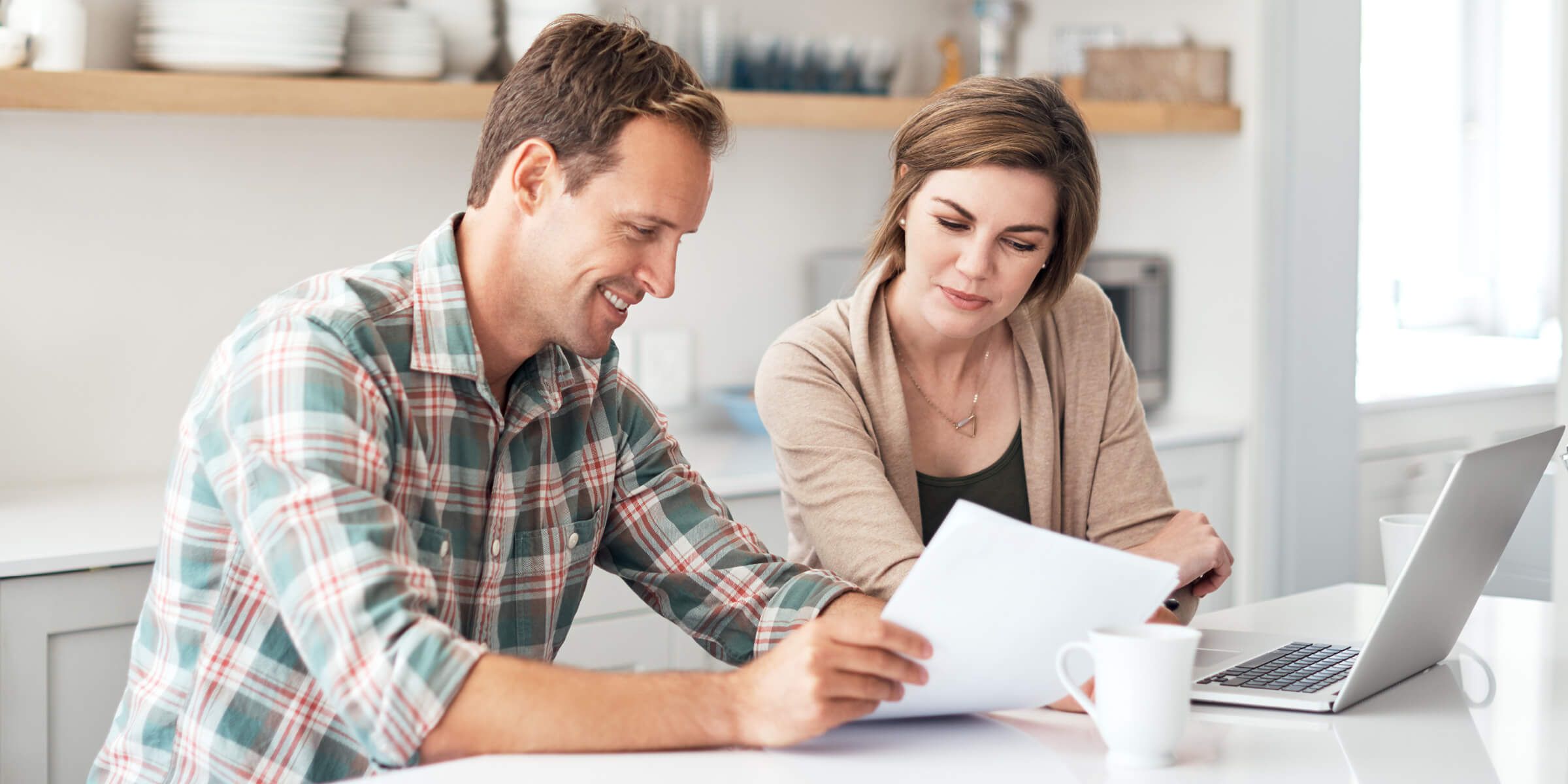 Couple sitting at table looking at paperwork in front of laptop
