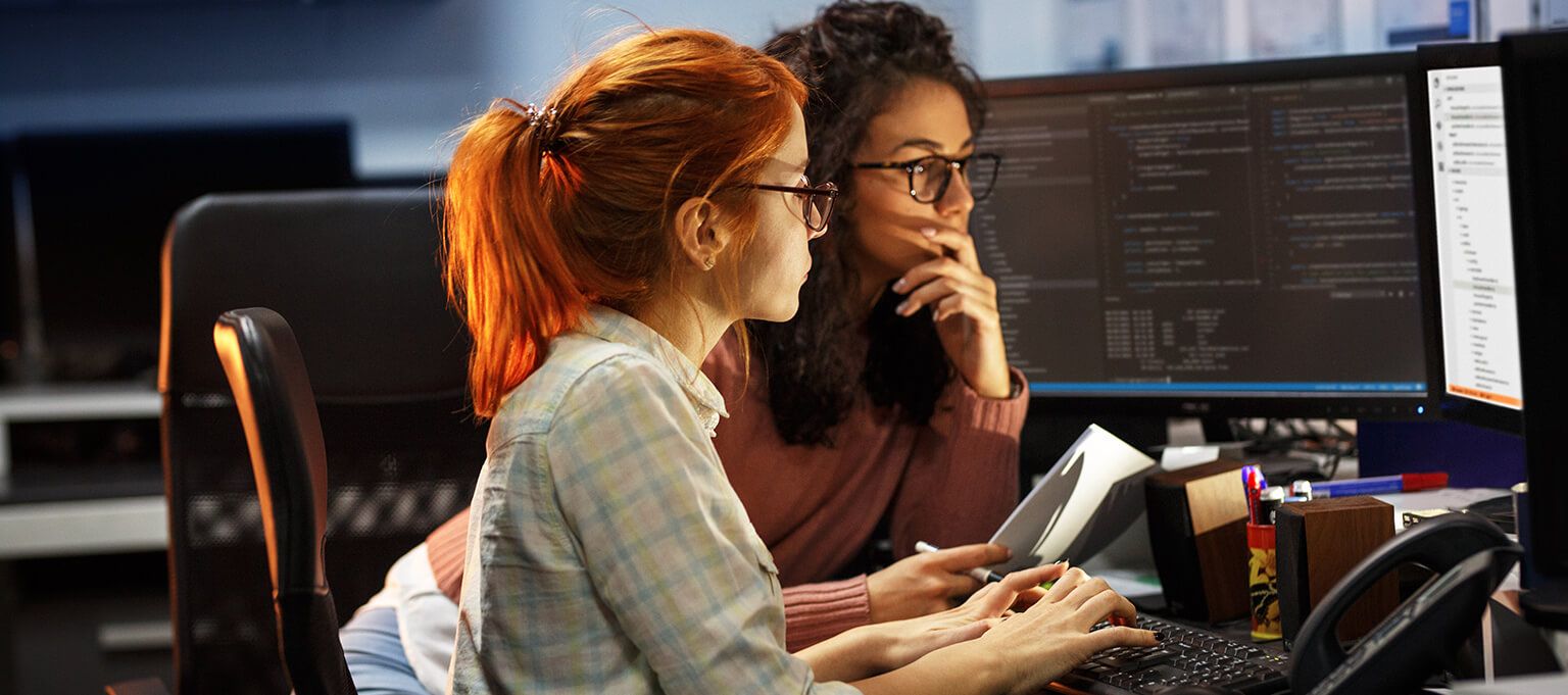 Two individuals working on computers in a tech office environment