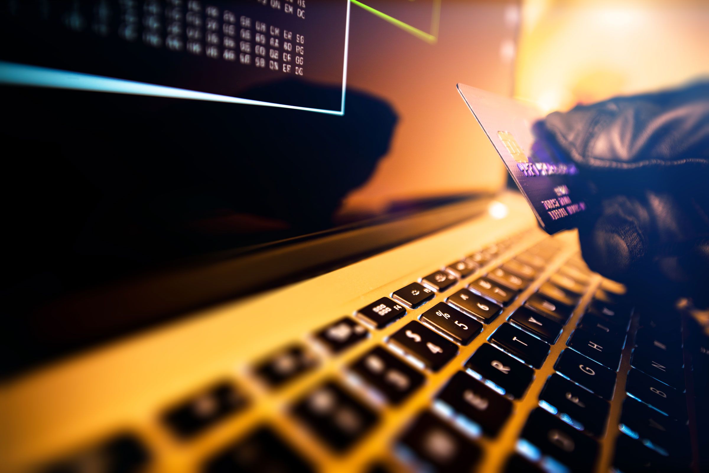 globed hand holding a credit card in front of a computer screen