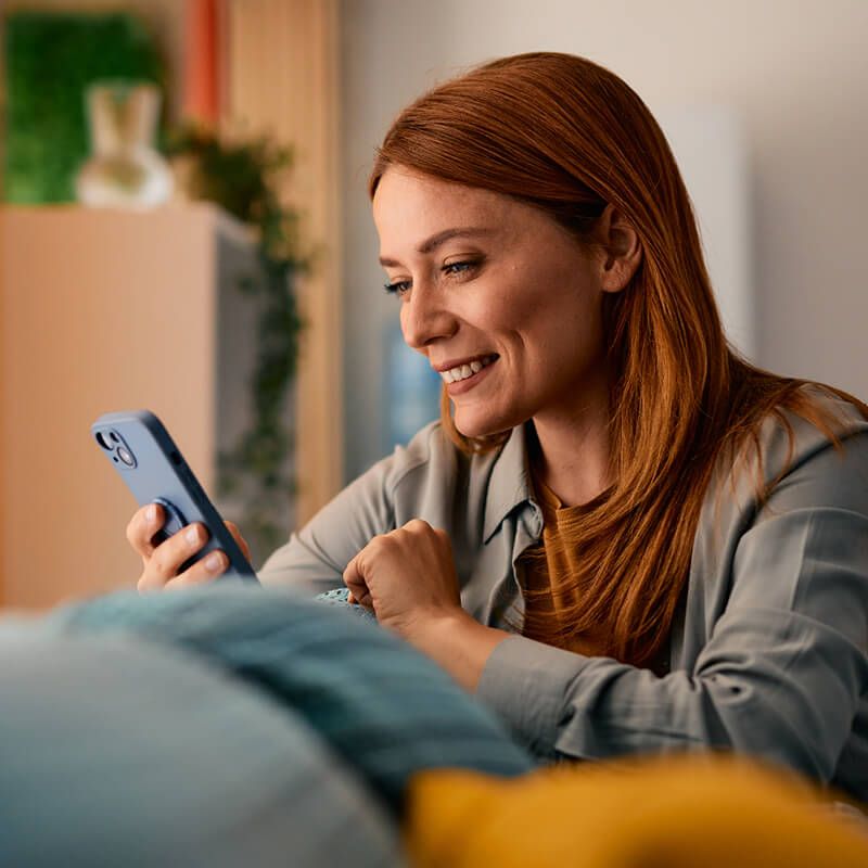 Happy woman relaxing on sofa using mobile phone at home.