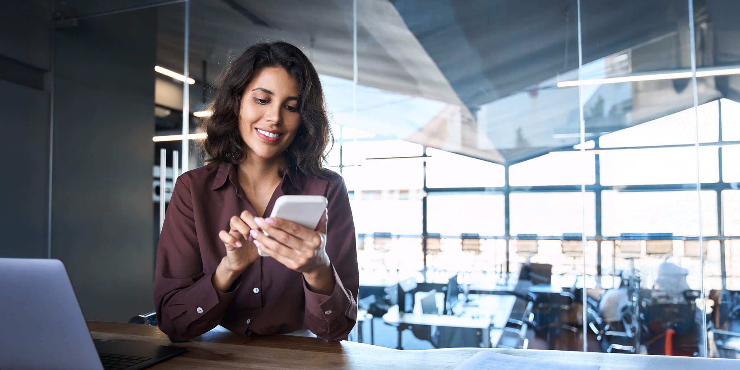 Young Indian business woman manager ceo using cell phone mobile app laptop. Smiling Latin Hispanic mature female businesswoman holding smartphone in office trading, reading, working online.