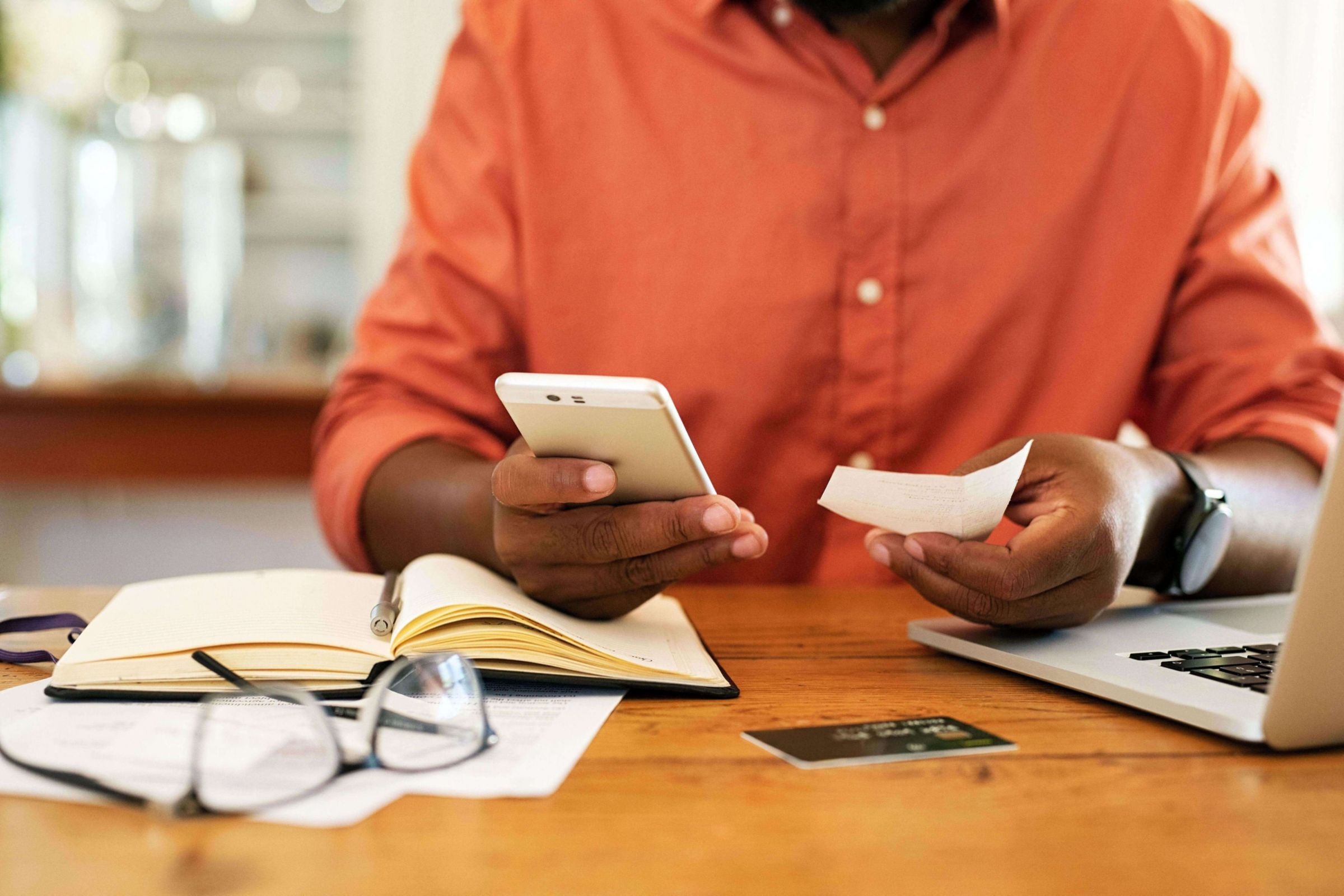 man holds a bill next to his smartphone