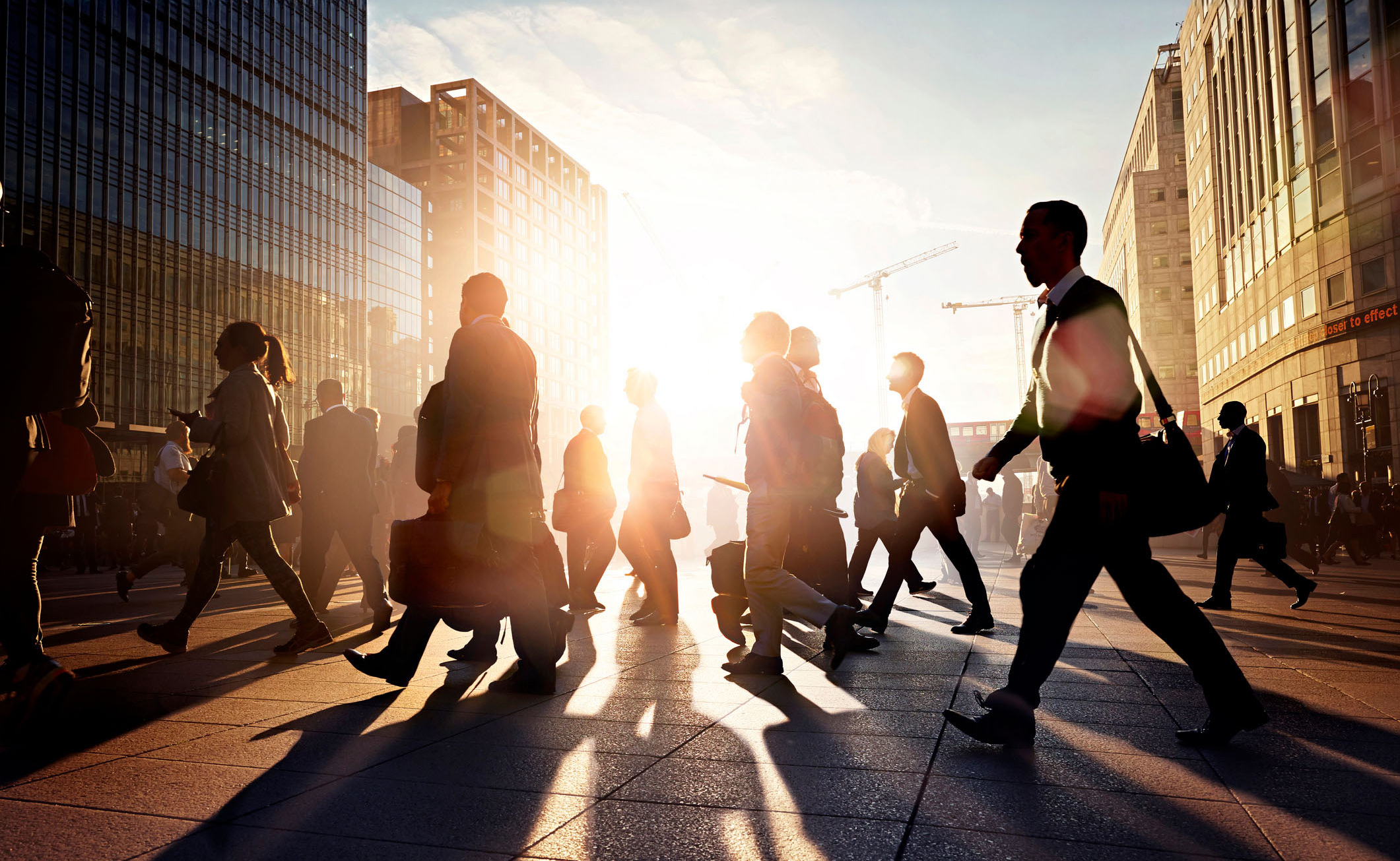Silhouettes of business commuters on a city street, backlit by the sun