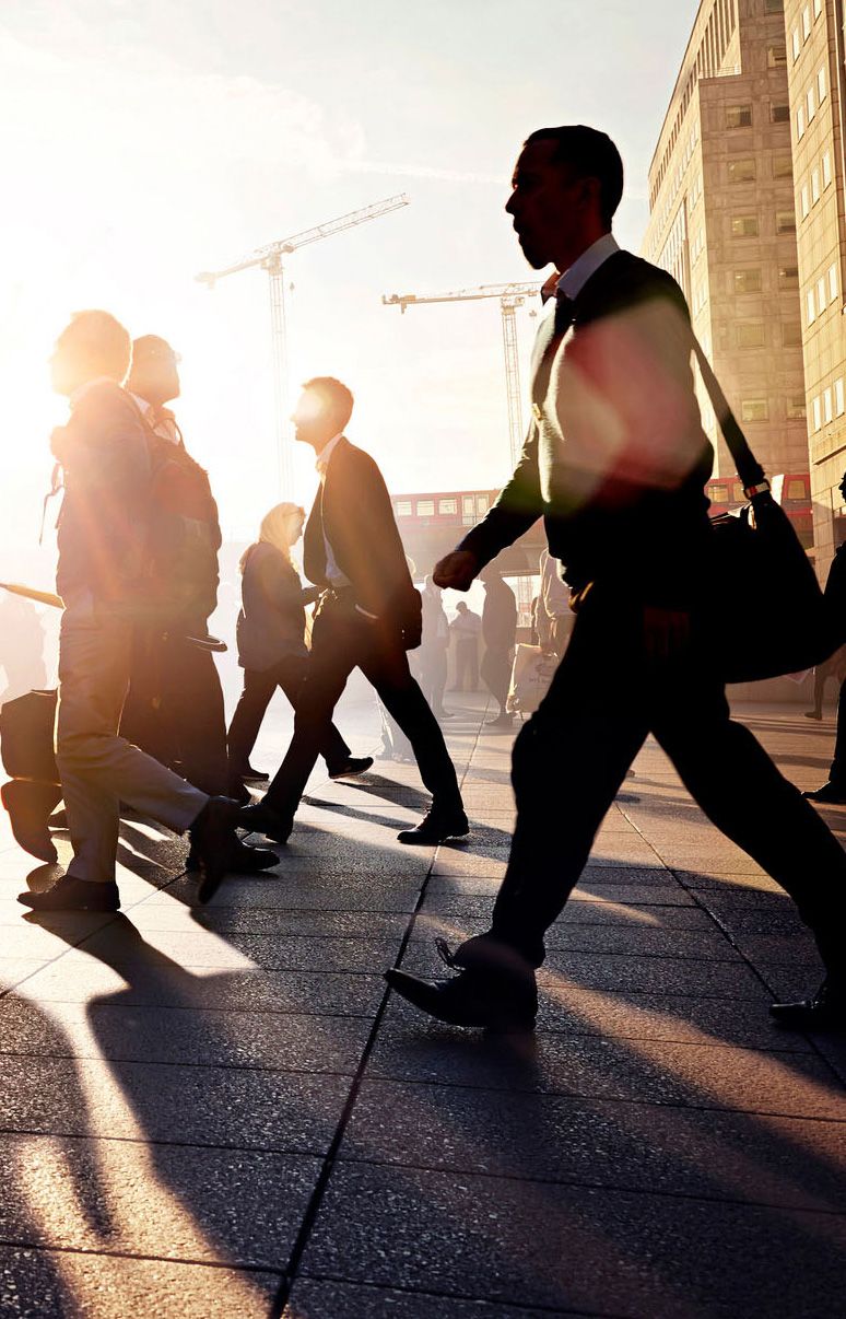 Silhouettes of business commuters on a city street, backlit by the sun
