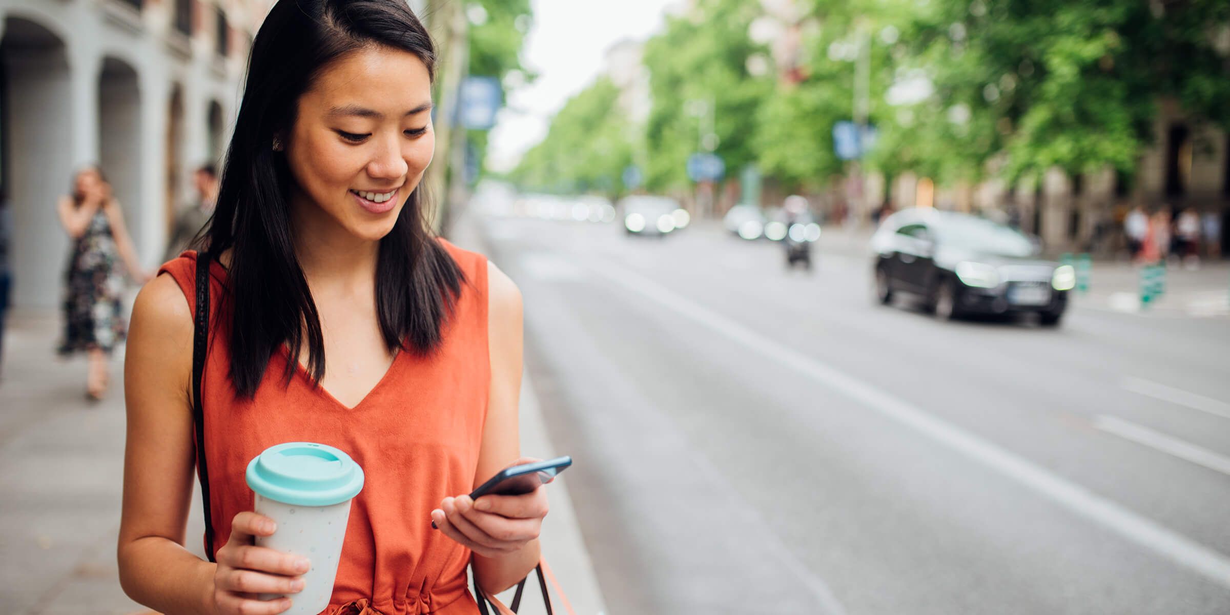 Happy young woman walking on the city street after shopping and using her smartphone