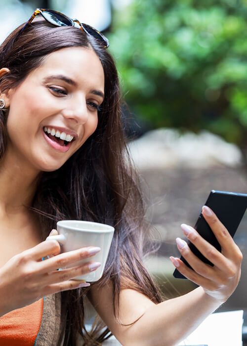 lady smiling at her phone while enjoying a cup of tea