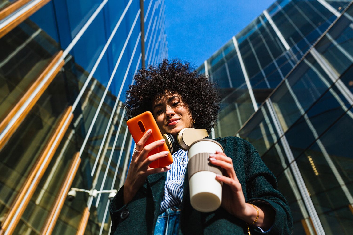 girl wialking in city holding a coffee looking at phone 