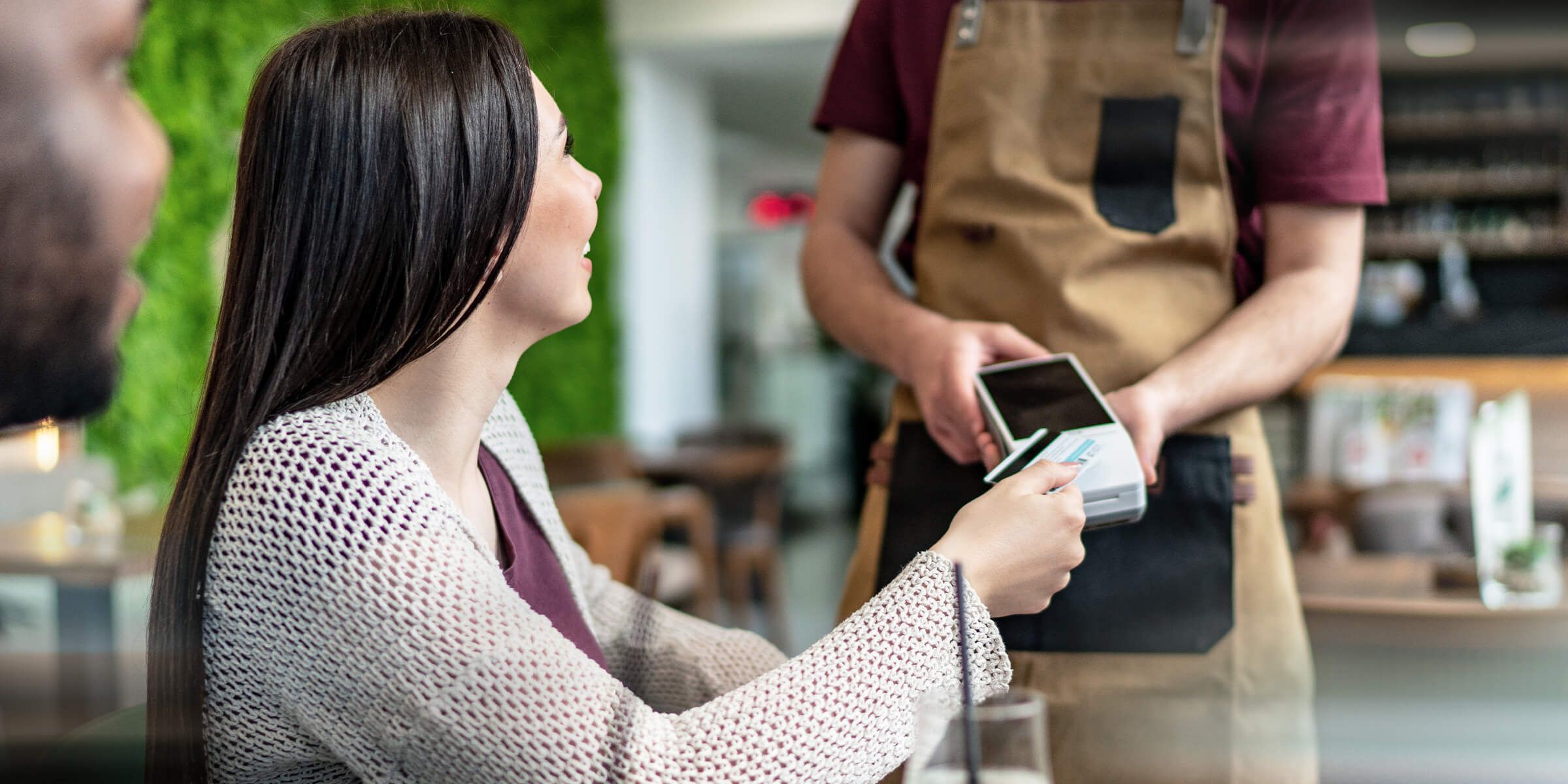A woman doing a touchless payment holds her card close to a compatible payment terminal