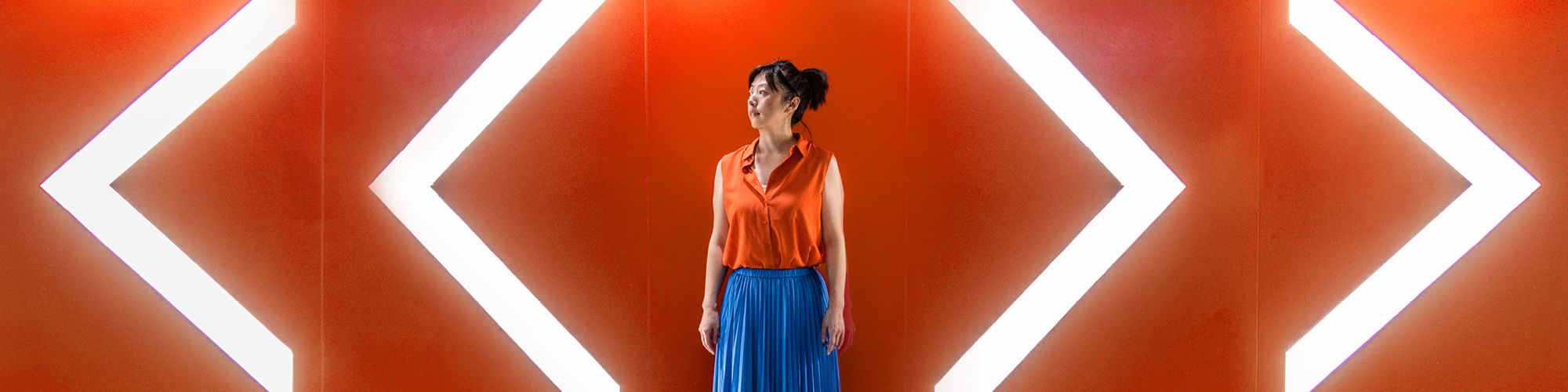 woman standing in front of an orange wall with large lighted arrows