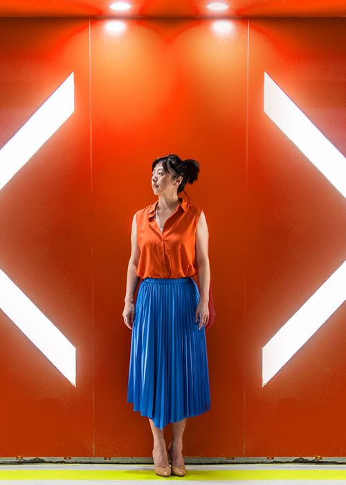 woman standing in front of an orange wall with large lighted arrows