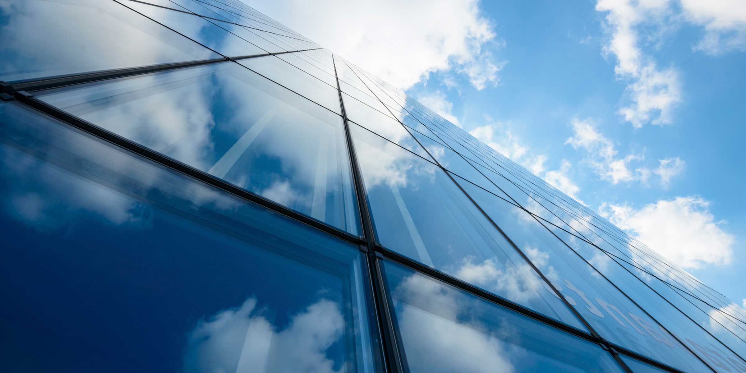 Reflective glass facade of a skyscraper against a blue sky with clouds