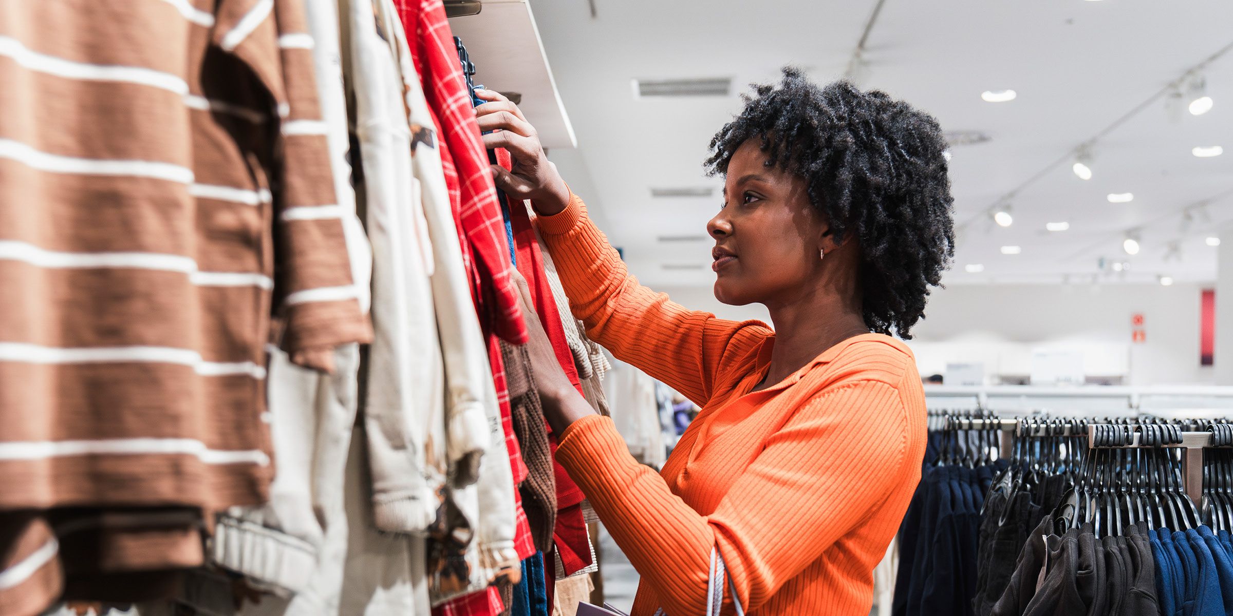 A woman is in a clothing store, browsing through clothes on a rack