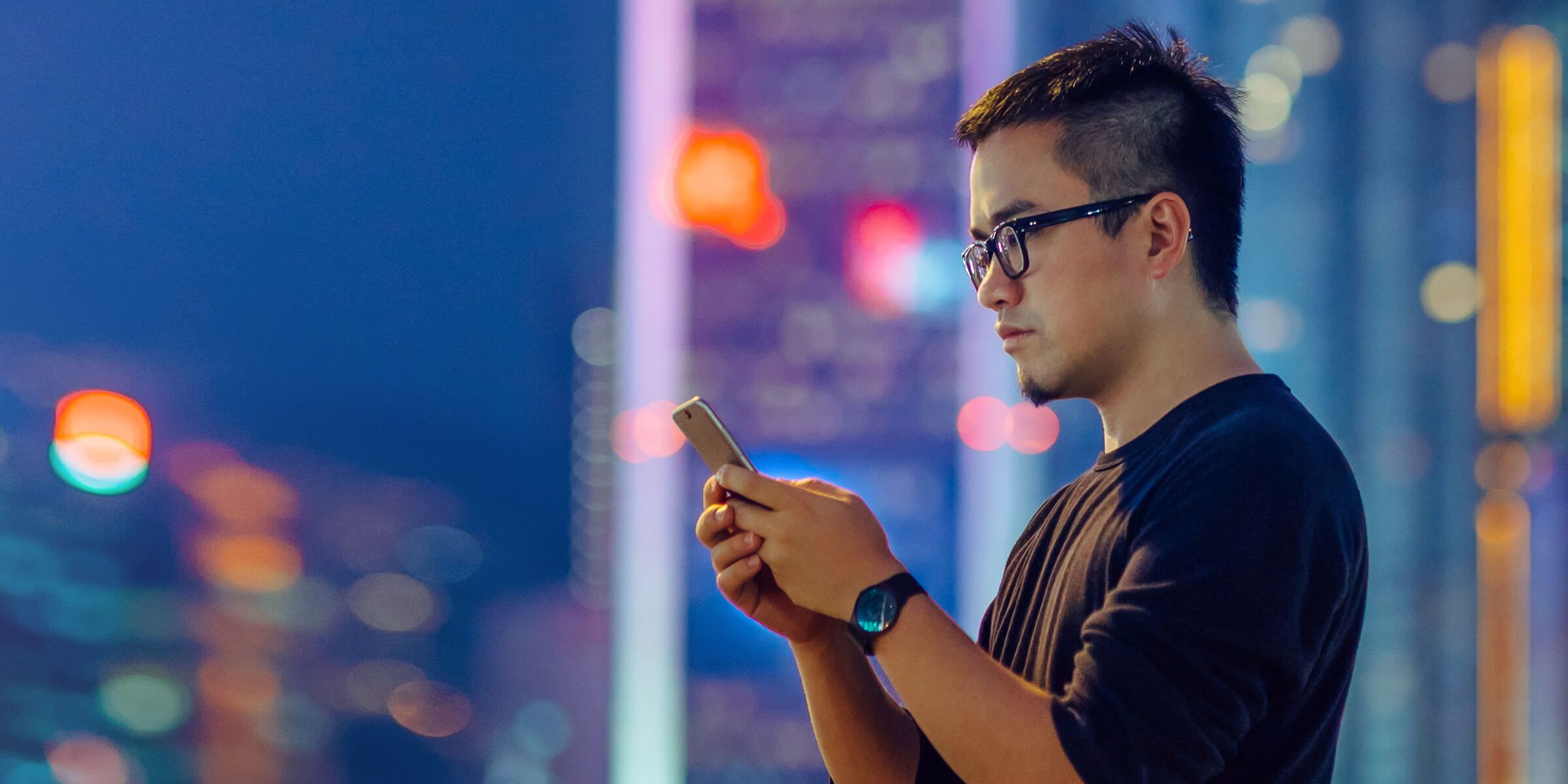 man texting on phone standing on city street in evening